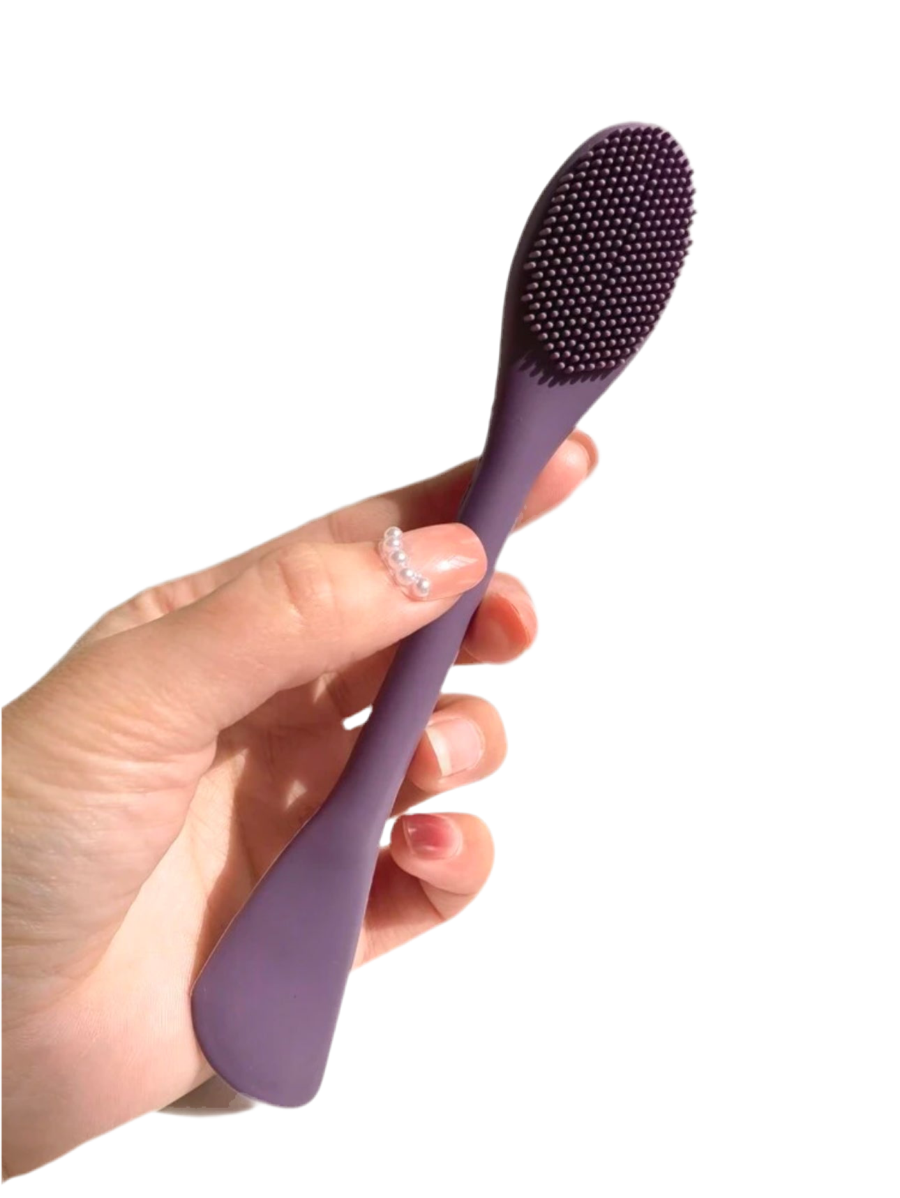 Hand holding a dual-ended silicone facial brush and spatula in purple color under natural sunlight